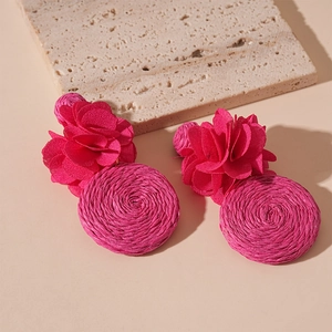 Detail of rose pink fabric flower and woven raffia round pendant on bohemian earring