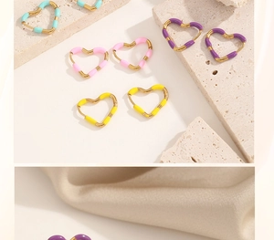 Flat lay of heart-shaped gold earrings with colorful pastel enamel on textured stone