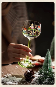 Detail of vintage glass goblet with green stem featuring hand-painted figures for Christmas