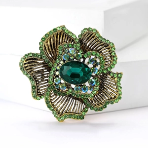 Macro view of vintage gold flower brooch with green rhinestones and oval center stone