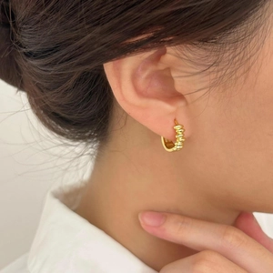 Close-up of elegant gold plated twisted hoop earrings worn by a model in warm light
