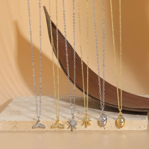 Detail view of 14K gold and silver plated fishtail and star necklaces on stone platform