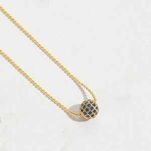 Detail of gold beaded necklace featuring a sphere pendant with pavé blue zircon stones