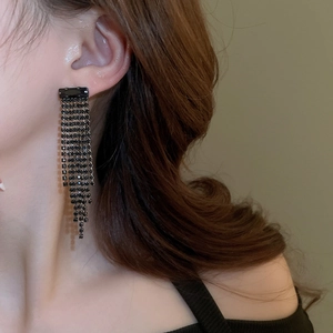 Close-up of long black rhinestone tassel earrings worn by a model in a luxury style