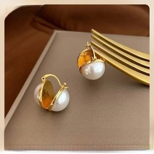 Artistic close-up of gold semi-circle pearl earrings hanging on a vintage metal fork