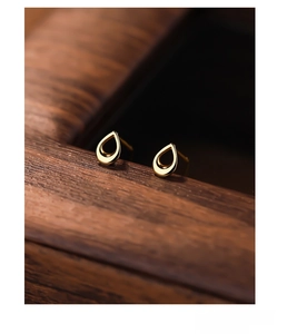 Macro shot of gold-plated S999 sterling silver teardrop studs on a dark wooden surface
