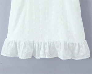 Close-up of white dress showing intricate eyelet embroidery and ruffled hem details