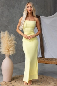 Detail of a slim fit pale yellow backless maxi dress with crossed straps in a minimalist room