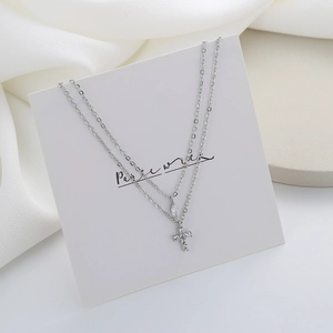 Detail of silver double-layered necklace with zircon teardrop and pavé cross charm