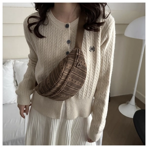 Detail of dark brown knitted crossbody bag with wide strap on beige cardigan