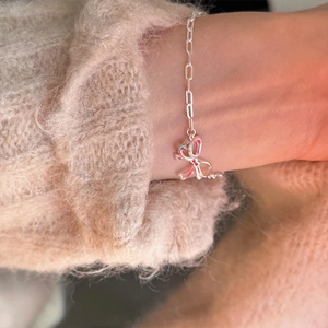 Close-up of a silver bow knot bracelet on a wrist with a soft sweater background