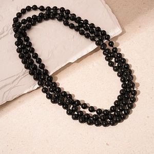 Close-up of triple-layer black beaded necklace on a textured white stone display stand