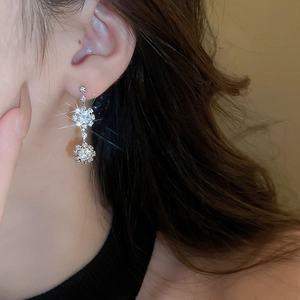 Close-up of sparkling silver snowflake earrings with round crystal pendants on a model
