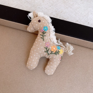 Detail of vintage horse brooch featuring floral embroidery and cotton fringe textures