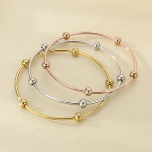 Detailed view of three polished metal bangles in gold, silver, and rose gold with moving beads
