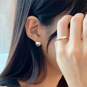 Detail of silver S925 heart earrings and spiral ring worn on skin showing metallic shine