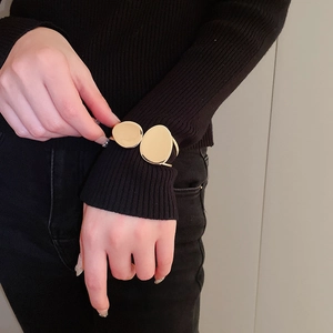 Detail of minimalist gold double-disc open bangle worn over a black sweater sleeve