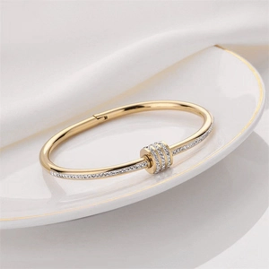 Detail of a gold stainless steel hinged bracelet featuring crystal-encrusted rings on silk