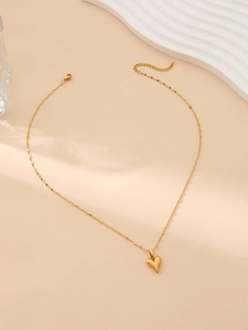 Detail of a golden stainless steel heart pendant necklace on a textured beige surface