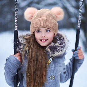 Close-up of beige knit winter hat with dual pink faux fur pom poms worn by girl