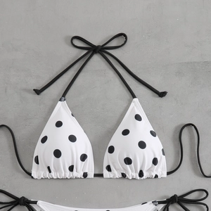 Detail of polka dot bikini top with halter ties on a textured grey background