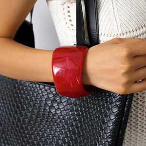 Detail of red wide resin bangle with marble texture worn by model with woven bag