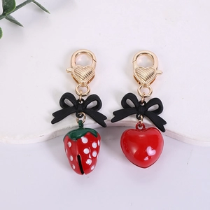 Detail of red strawberry and heart keychains with black bows and golden lobster clasps