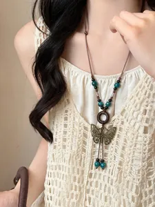 Close-up of bronze butterfly pendant with wood ring and green beads on woven cord