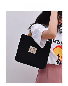 Close-up of black canvas tote bag with brown woven handles and cute bear patch detail