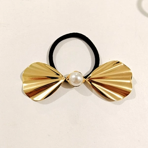 Detail of a golden metal bow hair accessory with a pearl center on a black elastic band