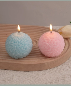 Close-up of lit rose embossed sphere candles in pink and blue on a wooden tray