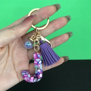 Detail of resin letter J keychain with purple tassel and glittering shell fragments