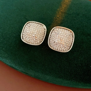 Macro shot of silver square stud earrings with pavé diamonds on green velvet fabric