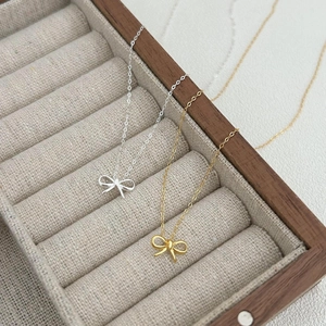 Minimalist 925 sterling silver bow necklaces in gold and silver finish on a linen jewelry box
