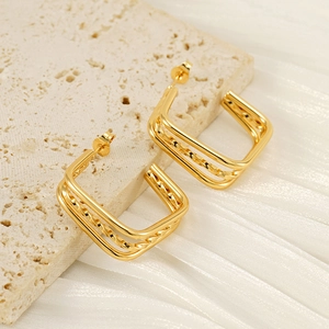 Polished gold square layered hoop earrings placed on a natural travertine stone surface
