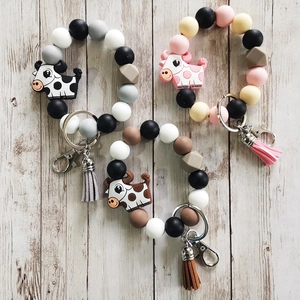 Silicone beaded key ring bracelets with cow charms and tassels on a wooden surface