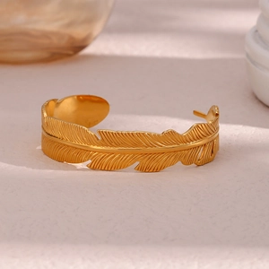 Detailed close-up of a 18K gold plated leaf cuff bangle on a soft pink marble surface