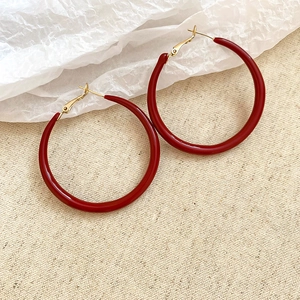 Detailed close-up of large round Ancora red enamel earrings with golden needle clips