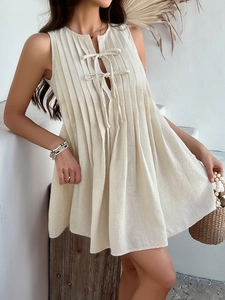 Detail of beige sleeveless pleated dress featuring a delicate neckline tie and linen texture