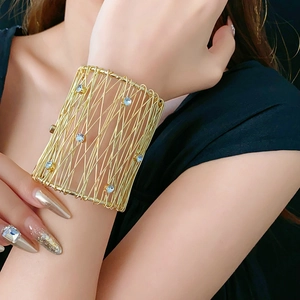 Detail of wide woven gold metal bracelet featuring intricate mesh and blue rhinestones