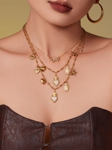 Detail of layered gold necklaces with bow and heart charms paired with large hoop earrings