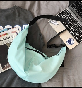 Light blue nylon crescent bag with adjustable strap styled on a desk with a laptop