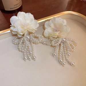 Close-up of white fabric flower earrings with elegant faux pearl tassels on a tray