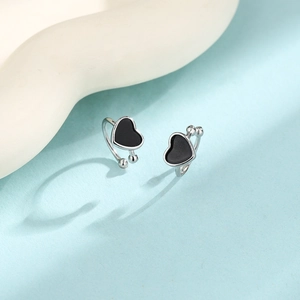Detail of silver heart ear cuffs with black enamel on a light blue background