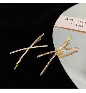 Detailed macro view of two golden X-shaped rhinestone hair clips on a reflective mirror