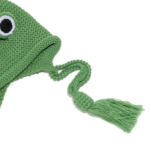 Detail shot of green knitted frog hat featuring textured ear flaps and tassel cords