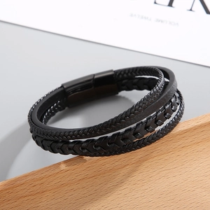 Detail view of multi-layer braided black leather bracelet with magnetic steel clasp on wood