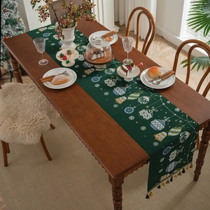 Green Christmas table runner with bells and tassels on a festive wooden dining table