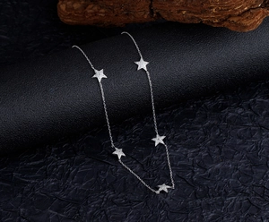 Detail of silver S925 necklace featuring five sparkling star charms on a dark surface