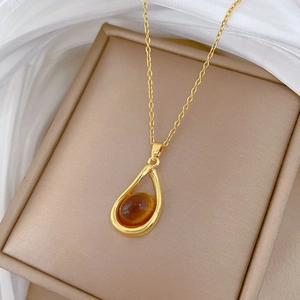 Detail of amber water drop pendant with diamonds on gold chain over silk fabric